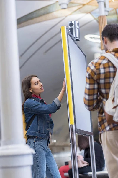 Vue arrière du touriste masculin avec sac à dos et sa petite amie regardant le panneau d'information à la station de métro — Photo de stock