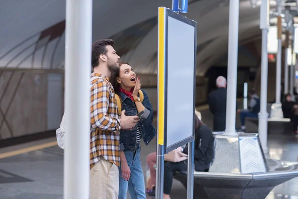 Vue latérale de touriste féminine surprise avec petit ami regardant le panneau d'information à la station de métro — Photo de stock