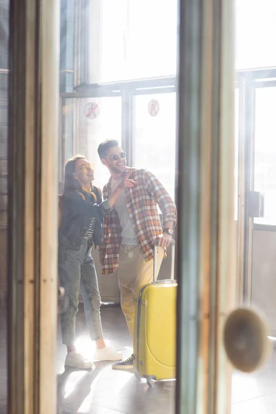 Female traveler pointing by finger to boyfriend with wheeled bag at subway — Stock Photo