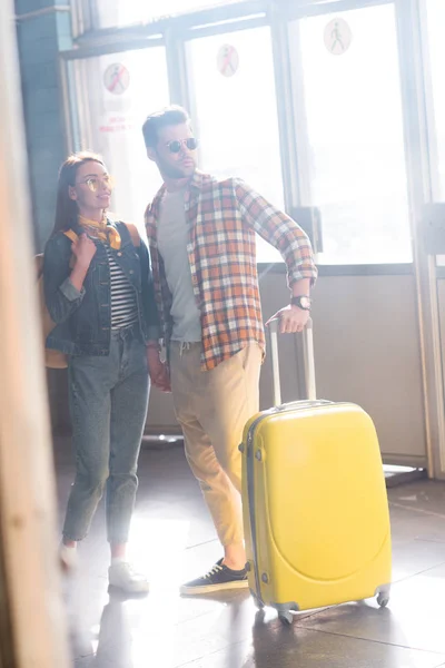 Stylish couple of tourists in sunglasses with backpack and wheeled bag at subway — Stock Photo