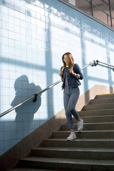 Young stylish female tourist in sunglasses with backpack going downstairs at subway — Stock Photo