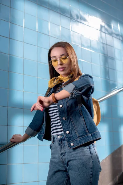 Junge stylische Touristin mit Rucksack und Sonnenbrille schaut auf die Armbanduhr — Stockfoto