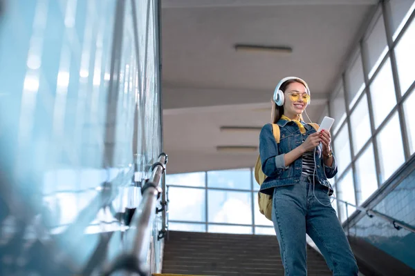 С низким углом зрения стильные женщины-туристки в солнечных очках с наушниками и смартфоном на лестнице в метро — стоковое фото