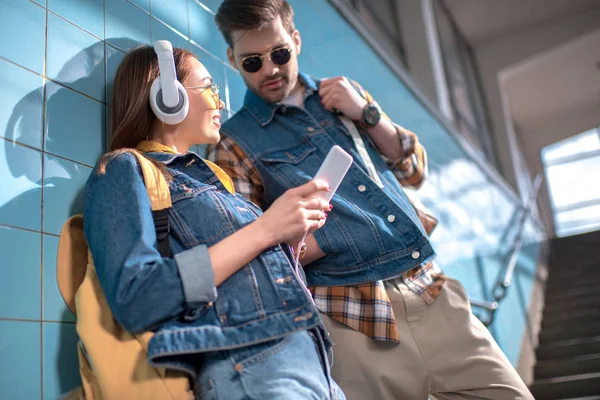 Souriant élégant touriste femelle avec écouteurs montrant smartphone à petit ami dans les lunettes de soleil — Stock Photo