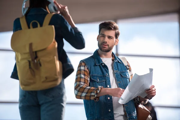 Élégant voyageur masculin avec carte à la main demandant de l'aide femme avec écouteurs et sac à dos au métro — Photo de stock