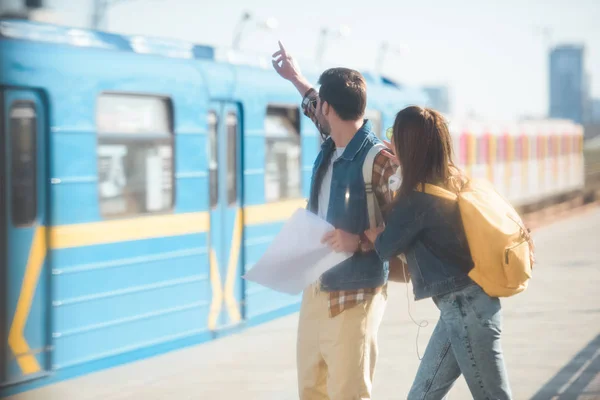 Stylish male tourist with arm raised and girlfriend at outdoor subway station — Stock Photo