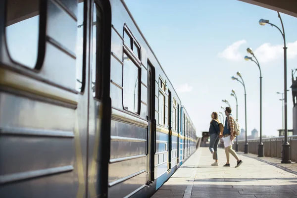 Vista lejana de un par de turistas con mochilas entrando en tren en la estación de metro al aire libre - foto de stock