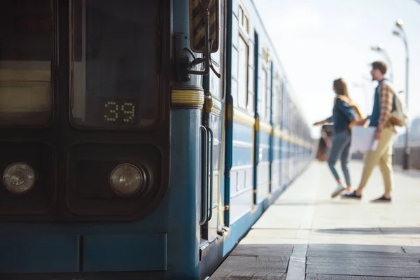 Крупним планом поїзд і пара туристів позаду на відкритій станції метро — стокове фото