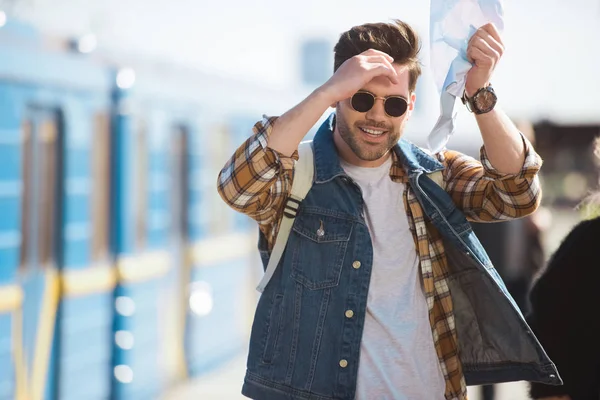 Stylish male traveler in sunglasses holding map in hand at outdoor subway station — Stock Photo