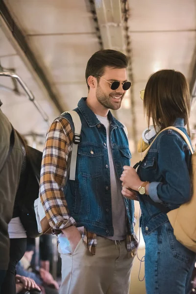 Sorridente viajante masculino em óculos de sol conversando com namorada no trem do metrô — Fotografia de Stock