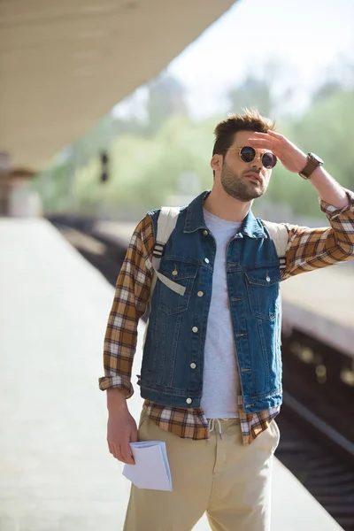 Stylish male tourist in sunglasses with map in hand waiting train at outdoor subway station — Stock Photo
