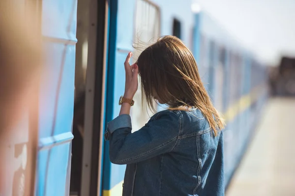 Vista lateral de la mujer con estilo con reloj de pulsera que entra en tren en la estación de metro al aire libre - foto de stock