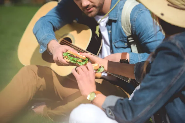 Plan recadré de voyageuse donnant sandwich au petit ami avec guitare acoustique — Photo de stock