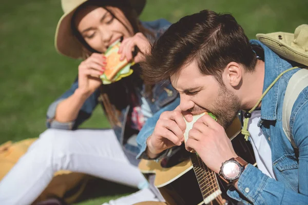 Couple of stylish travelers with guitar eating sandwiches — Stock Photo