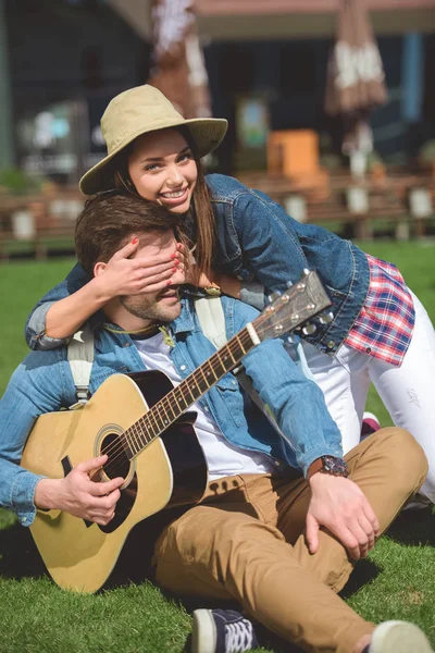 Female tourist in hat covering eyes of boyfriend with guitar from behind — Stock Photo