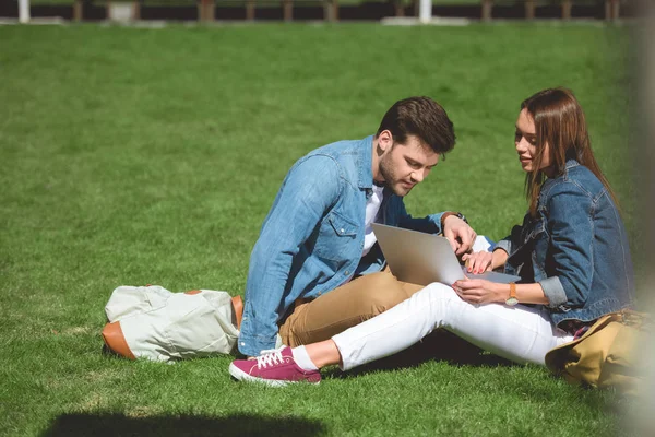 Joven pareja de viajeros con mochilas usando portátil en la hierba - foto de stock