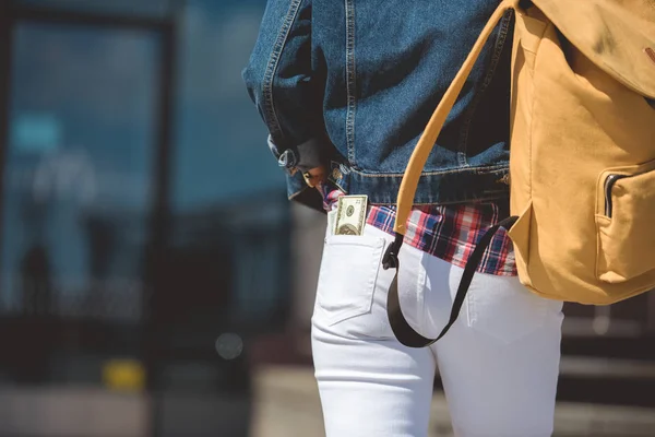 Tiro recortado de turista feminino elegante com mochila e nota de dólar no bolso de jeans — Fotografia de Stock
