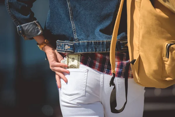 Image recadrée de touriste féminine élégante avec sac à dos et billet en dollar dans la poche de jeans — Photo de stock