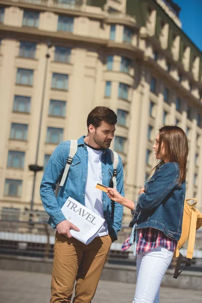 Turista mujer dando tarjeta de crédito a novio con periódico de viaje en la mano - foto de stock