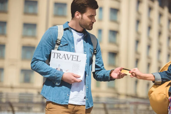 Cropped image of female tourist giving credit card to boyfriend with travel newspaper in hand — Stock Photo