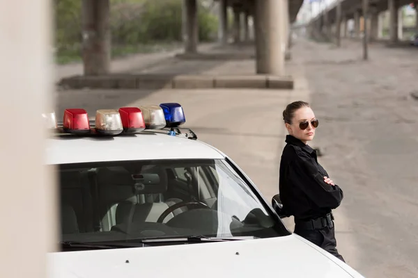 Policial feminino com braços cruzados apoiados em carro de patrulha — Fotografia de Stock