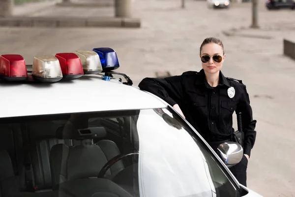 Policial feminino apoiando-se em carro de patrulha — Fotografia de Stock