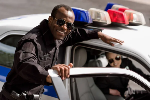 Happy young police officers with car looking at camera — Stock Photo