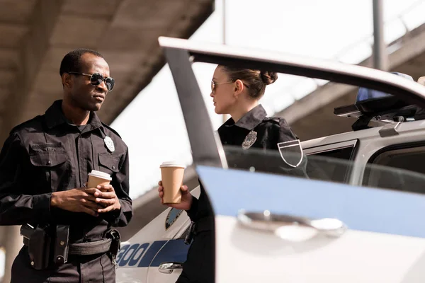 Young relaxing police officers drinking coffee near police car — Stock Photo