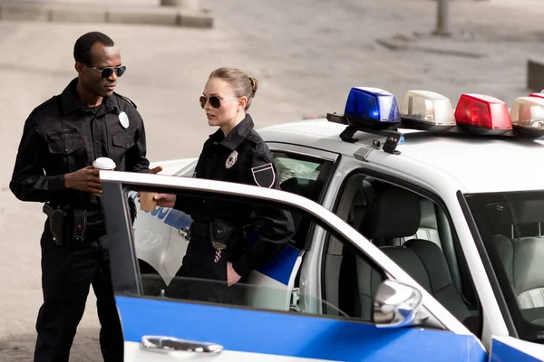 Young male and female police officers drinking coffee near police car — Stock Photo