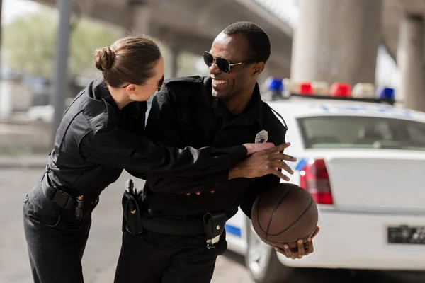 Young happy police officers having fun while playing basketball near car — Stock Photo