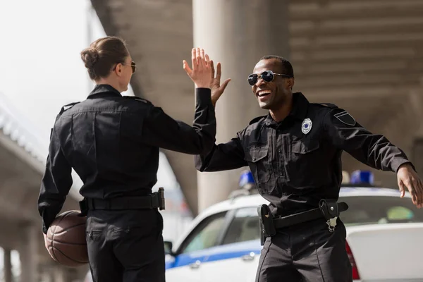 Oficiales de policía con pelota de baloncesto dando cinco altos - foto de stock