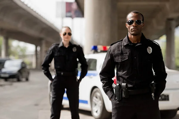 Police officers with hands in pockets looking at camera in front of car — Stock Photo