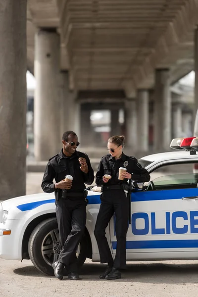 Police officers with coffee and doughnuts standing next to car — Stock Photo