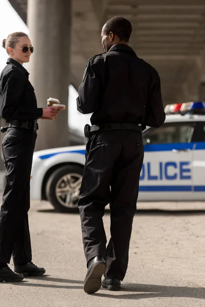 Policías sonrientes tomando un café y charlando delante del auto - foto de stock