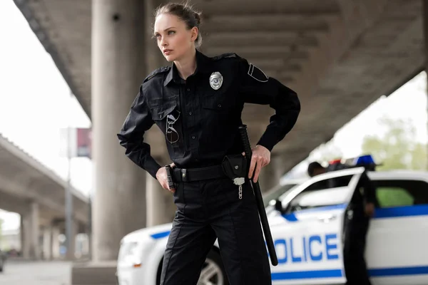 Confiada mujer policía mirando hacia otro lado y sacando arma y bate — Stock Photo