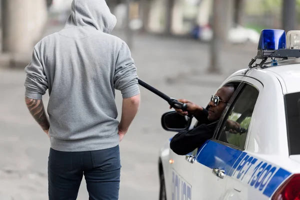 Задний вид африканского американского полицейского останавливает человека в капюшоне с полицейской битой, глядя в окно — стоковое фото