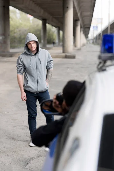 Policeman looking on hooded young man on street out of window — Stock Photo