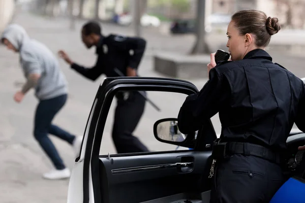 Policewoman talking by radio set while her partner chasing thief — Stock Photo