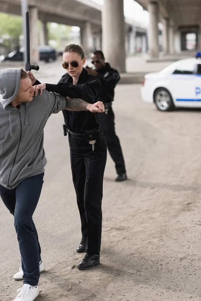 Mujer policía con porra arrestando a bandido y policía de pie detrás y apuntando con una pistola - foto de stock
