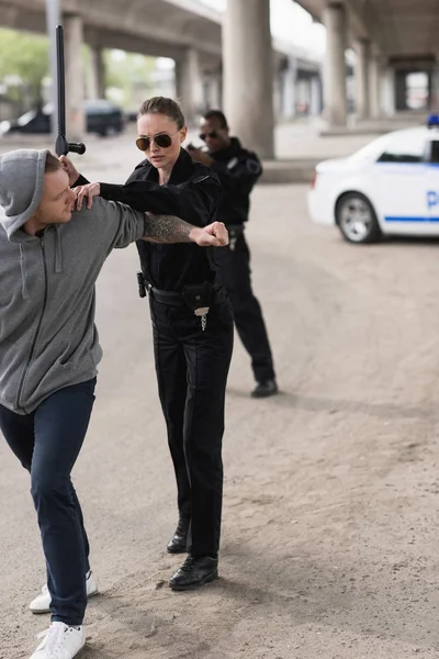 Policewoman with truncheon arresting bandit and policeman standing behind and aiming by handgun — Stock Photo