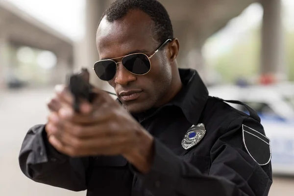 Portrait of african american policeman in sunglasses aiming by handgun — Stock Photo