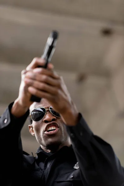 Vista de ángulo bajo del policía enojado gritando y apuntando con una pistola - foto de stock