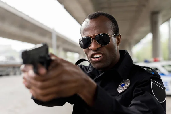 Policía afroamericano enojado gritando y apuntando con una pistola — Stock Photo
