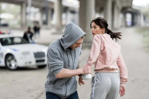 Robber in hoodie stealing handbag from shocked young woman — Stock Photo