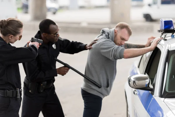 Policía afroamericana arrestando a un joven y a una mujer policía apuntando con una pistola - foto de stock
