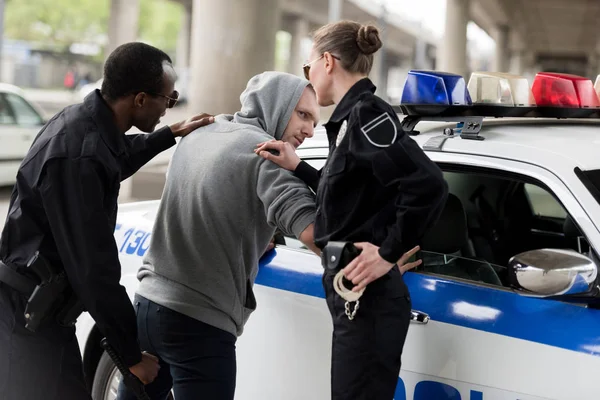 Policeman and policewoman arresting young man in hoodie — Stock Photo