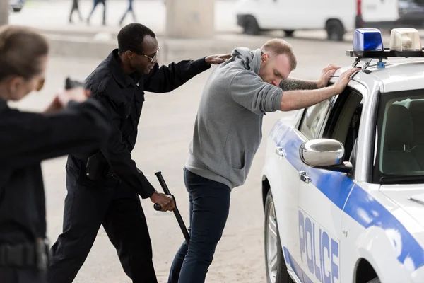 Vista lateral del hombre afroamericano arrestado mientras la policía le apuntaba con una pistola - foto de stock