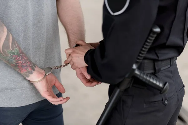 Cropped shot of policewoman with truncheon handcuffing bandit — Stock Photo