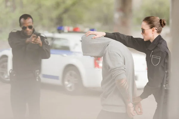 Женщина-полицейский держит преступника, а полицейский целится в него из пистолета. — стоковое фото