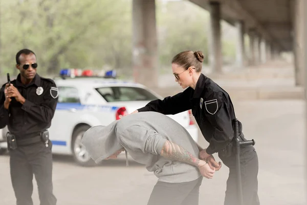 Oficiales de policía que arrestan a delincuente masculino con capucha - foto de stock